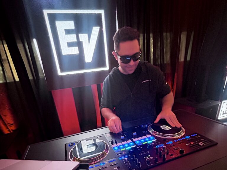 DJ JAS mixing on a DJ controller in front of the Electro-Voice logo