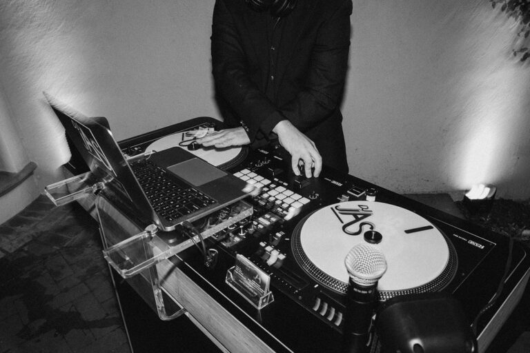 Black-and-white photo of DJ JAS with his hands on the decks at his DJ booth