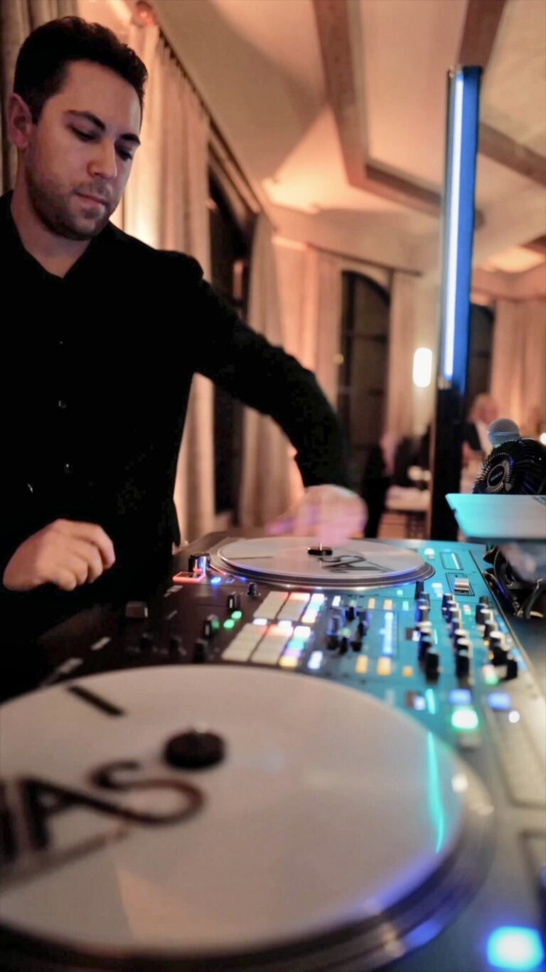 DJ JAS live mixing on turntables beside a glowing LED light column at a wedding